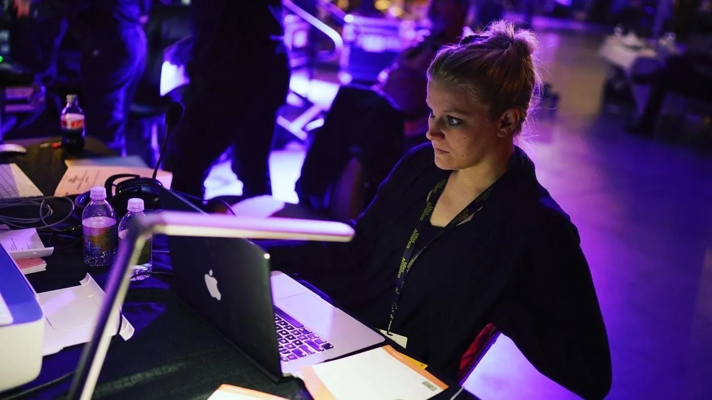 Susan working at a laptop backstage under purple light