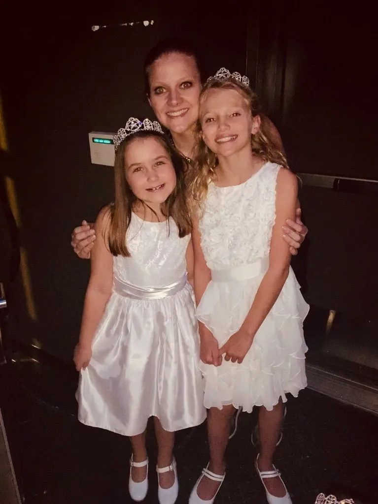 Susan backstage with two young girls in white dresses and tiaras