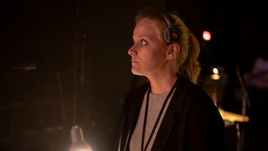 Susan wearing headphones backstage under warm light